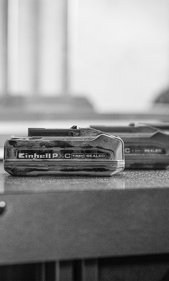 Black and white image of an Einhell Sealed Power-X-Change battery on a workbench in an industrial setting. 