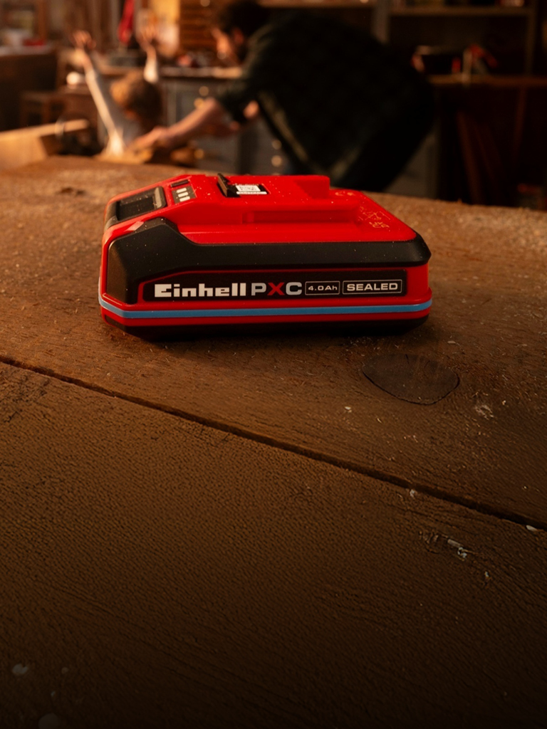 Батерия Einhell Power X-Change 4.0Ah SEALEAD върху дървена работна маса, показваща синия пръстен и етикет.