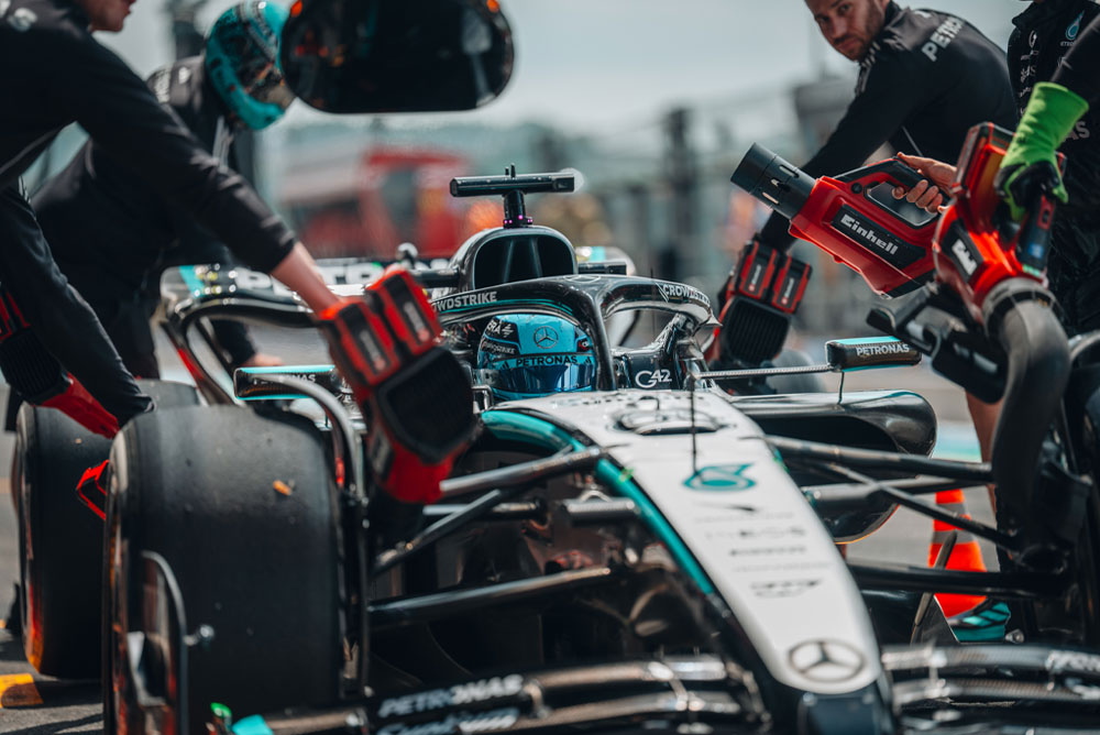 Автомобил на Mercedes-AMG PETRONAS Formula One Team по време на спиране в бокса. Членове на отбора използват безжични въздуходувки Einhell, за да охлаждат компонентите на автомобила. Екипът е фокусиран и работи с прецизност.