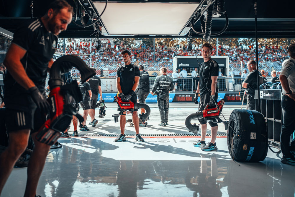 Механиците на Mercedes-AMG PETRONAS Formula One Team се подготвят в гаража с безжични въздуходувки Einhell преди спиране в бокса. На заден план трибуните са пълни с фенове.