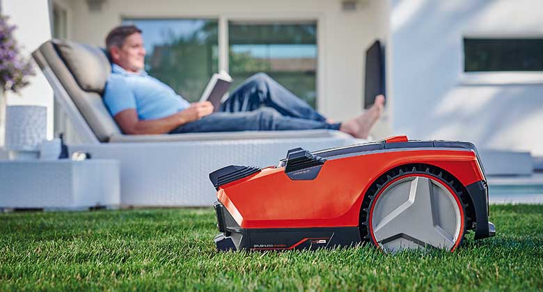 lawn mower robot mows the lawn and man lies in the background
